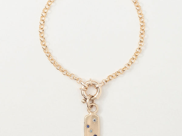 A gold bracelet with a rectangular pendant featuring a star-speckled gemstone, designed to represent a zodiac constellation.
