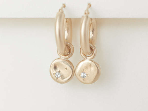 A pair of small gold hoop earrings with starry night charms attached, displayed against a white background.