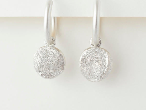 A pair of sterling silver hoop earrings with puppy print textures, displayed against a white background.