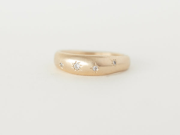 A smooth, dome-shaped gold ring with curved edges and small embedded sparkling stones arranged in a starry-night pattern