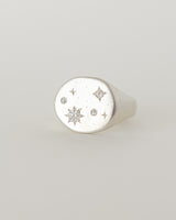 A silver signet ring with a starry night design, featuring a central diamond or moissanite gem surrounded by smaller stones, and engraved details on the band.