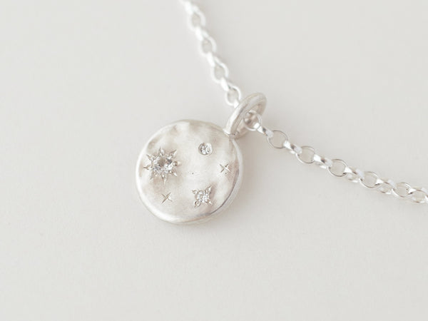 A silver necklace featuring a molten silver disc with three scintillating stones surrounded by hand-engraved 4-point stars, attached to a chunky belcher chain.