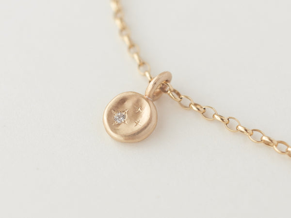 A close-up of a mini starry night necklace with a molten gold disc and a small diamond or moissanite stone, hanging on a chain.