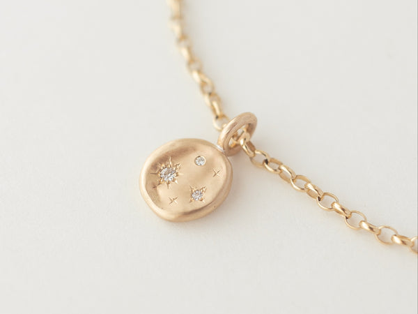 A medium-sized gold necklace with a disc pendant featuring three small, inset gemstones, displayed against a light background.