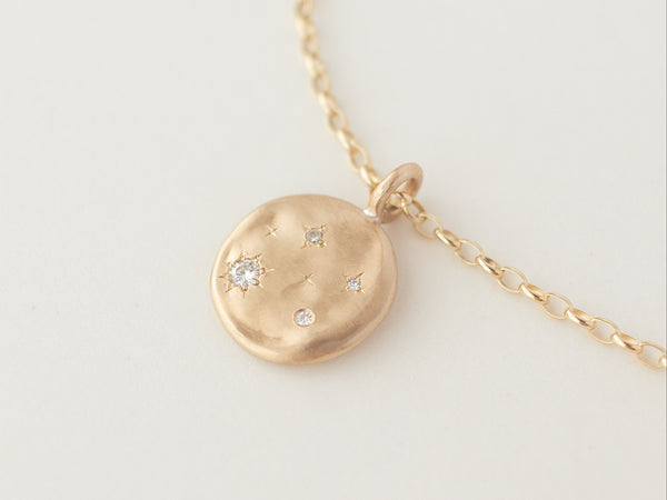 A gold necklace with a round pendant featuring a molten gold disc with four Diamonds or Moissanites surrounded by hand-engraved 4-point stars.