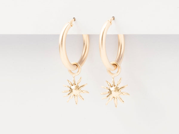 A pair of gold hoop earrings with gold sun charm attachments on a white background.