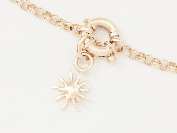 A close-up image of a gold charm necklace featuring a small gold sun charm on a gold chain.