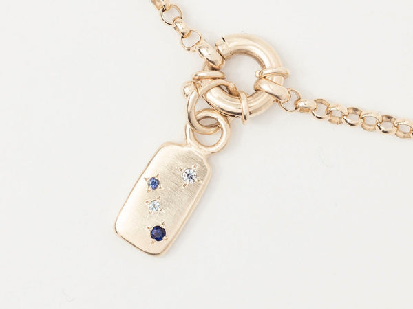 A gold chain necklace with a rectangular charm featuring a row of blue star-set gemstones.