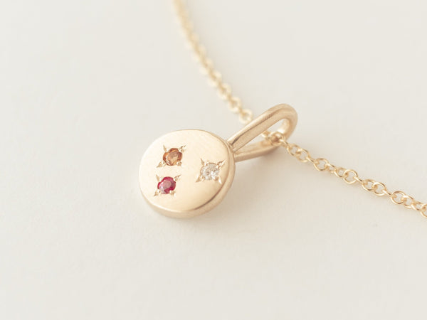 A gold necklace featuring a recycled gold pendant with three gemstones set in a 4 point star configuration, displayed on a white background.