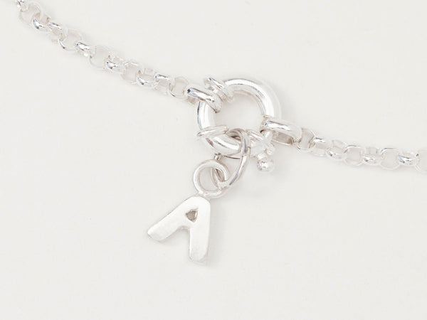 A silver letter charm attached to a bold belcher chain necklace, with a small connector next to the charm.