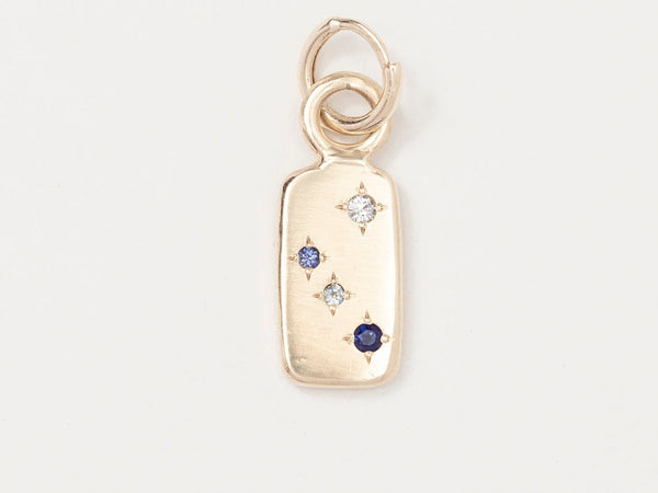 A gold rectangle charm with a series of blue star-shaped gemstones on it.