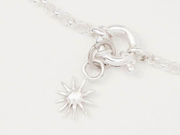 A silver necklace featuring a small silver sun charm attached to a sterling silver chain with a small connector.