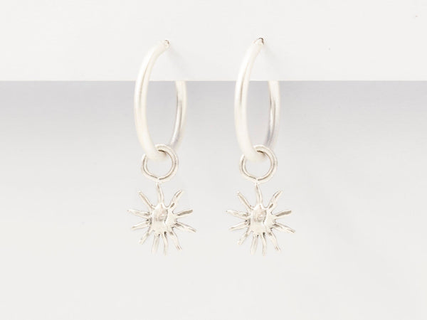A pair of silver hoop earrings with small sun charm pendants attached to them, displayed against a white background.